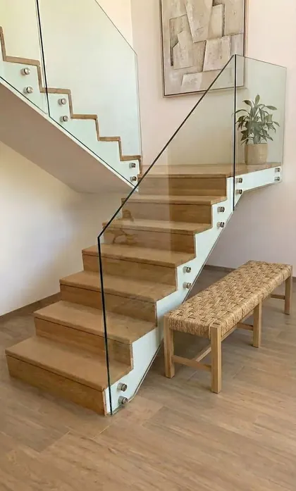 Escalera de madera con baranda de vidrio y banco de fibra tejida en el hall de planta baja