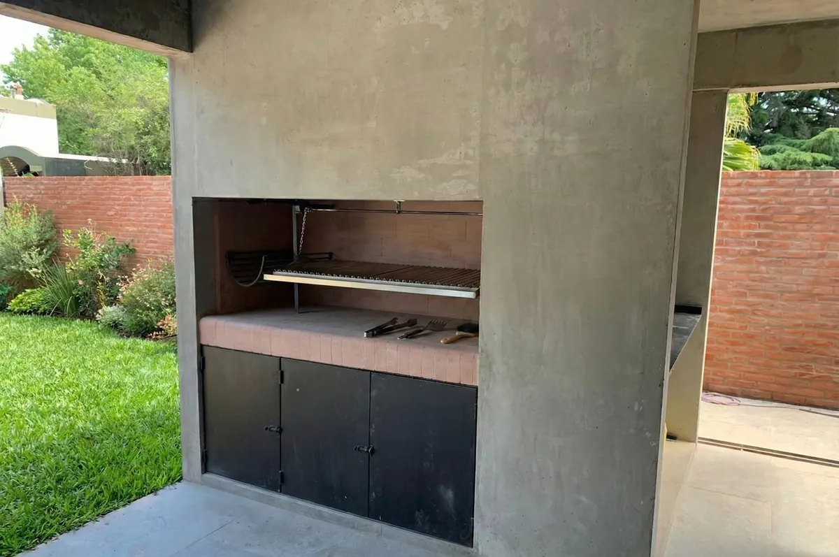 Parrilla de hormigón bajo la galería, con mesada de ladrillo y puertas de chapa negra