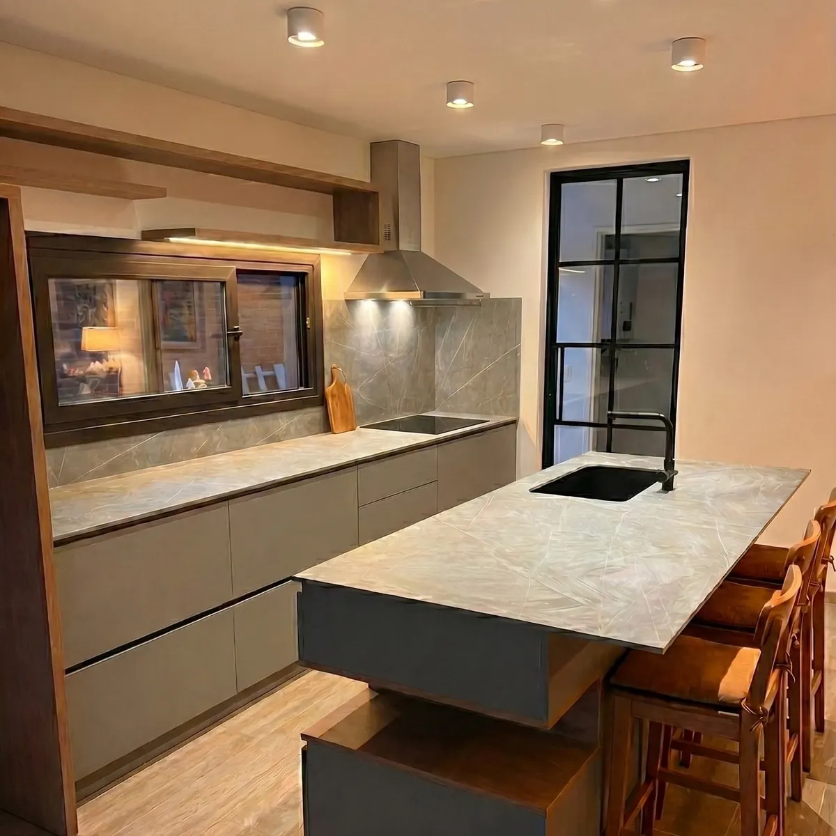 La cocina con isla y la ventana pasaplatos de marco negro hacia la galería